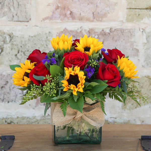 Red roses and yellow sunflowers in a glass vase with burlap ribbon