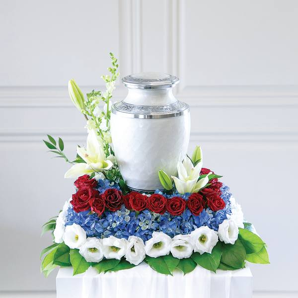 Floral urn arrangement with red roses, blue hydrangeas, and white lilies