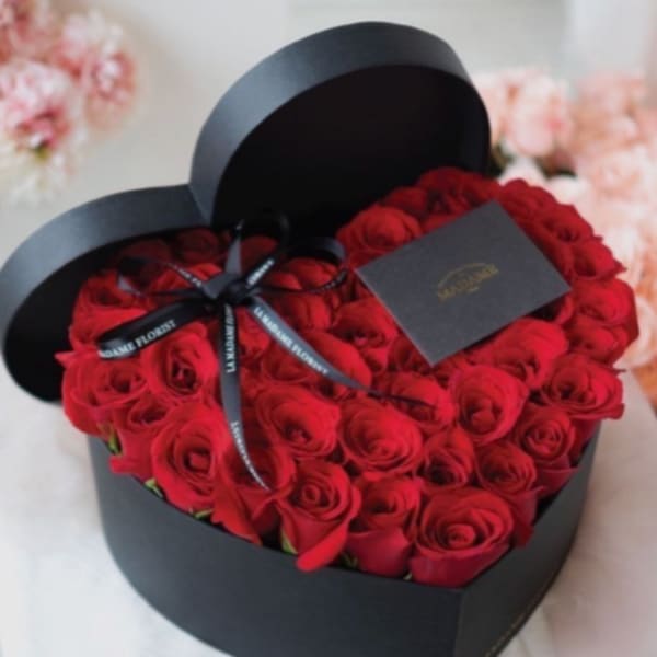 Red roses arranged in a black heart-shaped box with a ribbon and card