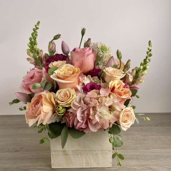 Mixed pink and peach flower arrangement in a white wooden box
