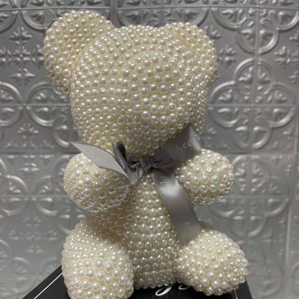 Pearl-covered teddy bear with a ribbon on a black box