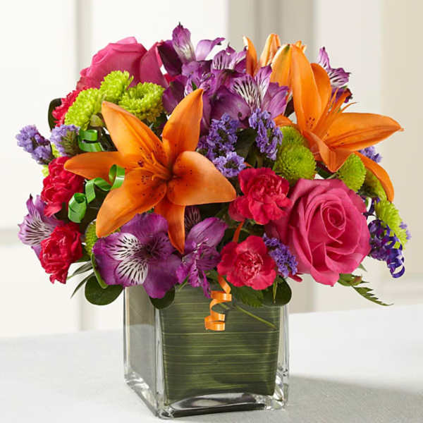 Bright mixed bouquet with orange lilies, pink roses, and purple flowers in a glass vase