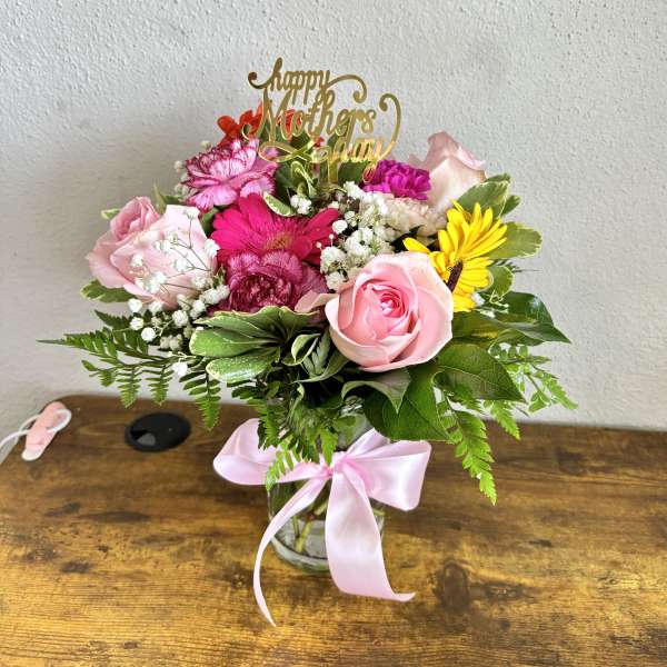 Pink and yellow mixed bouquet in a glass vase with a Mother’s Day topper
