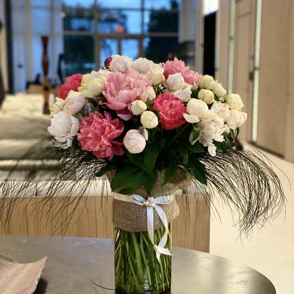 Pink and white peonies in a glass vase with a ribbon wrap