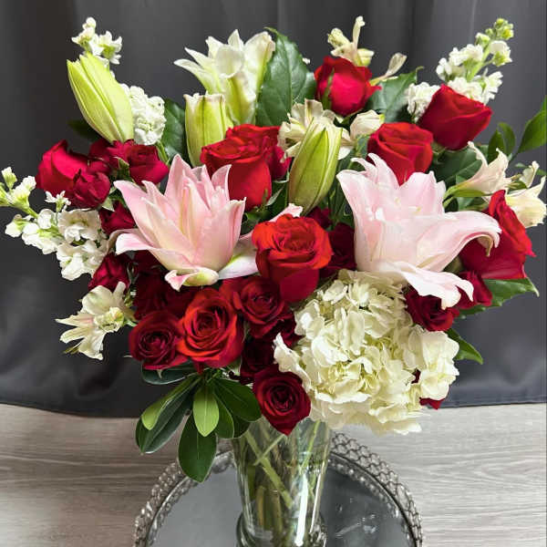 Bouquet of red roses, pink lilies, and white hydrangeas in a glass vase