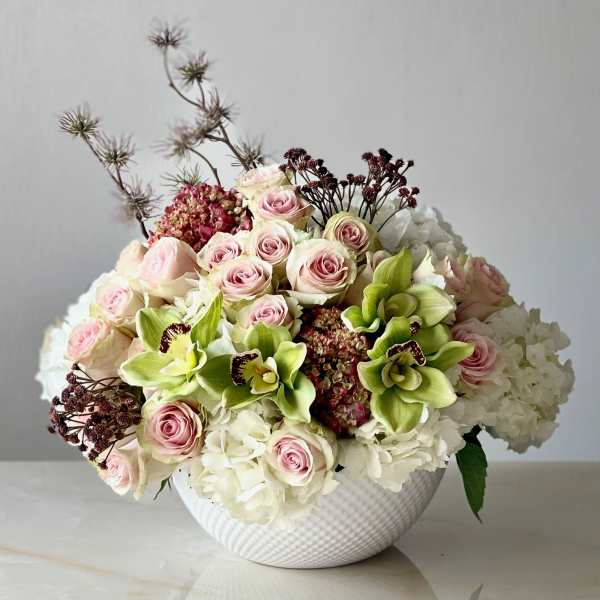Bouquet of pink roses, white hydrangeas, and green orchids in a white vase