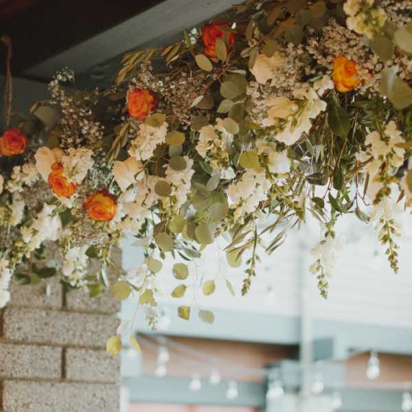 Hanging floral arrangement with orange and white roses and trailing greenery