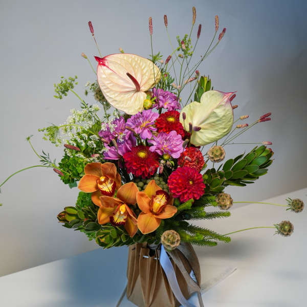 Colorful mixed bouquet with orchids, anthuriums, and dahlias in a wrapped base