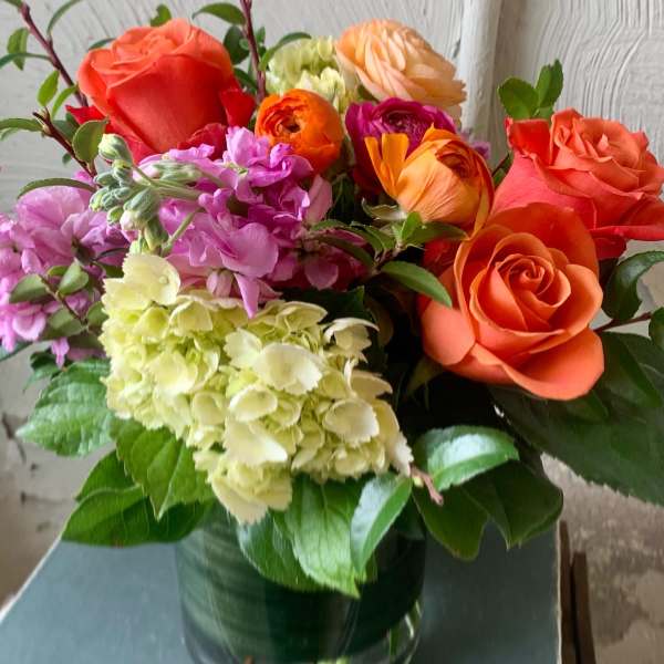 Mixed bouquet of orange roses, hydrangeas, and pink flowers in a glass vase
