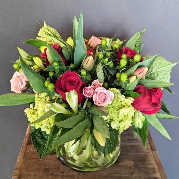 Mixed bouquet of roses, lilies, and green berries in a glass vase
