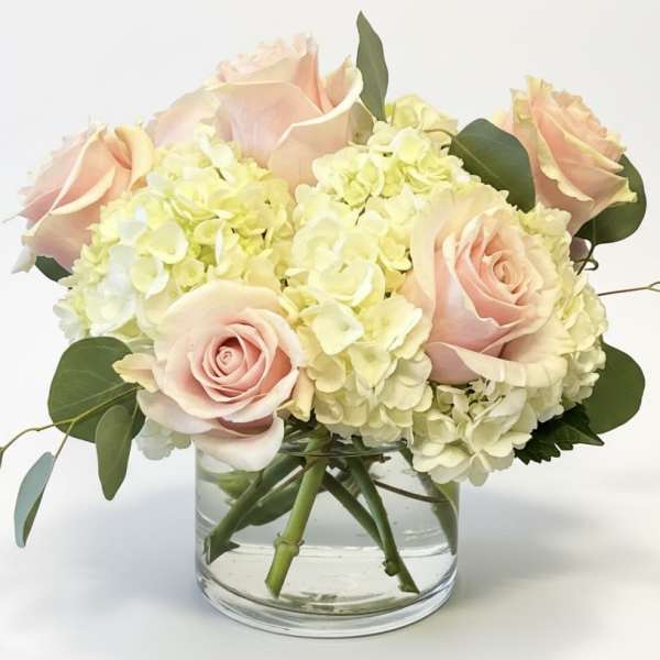 Blush roses and pale hydrangeas in a clear glass vase