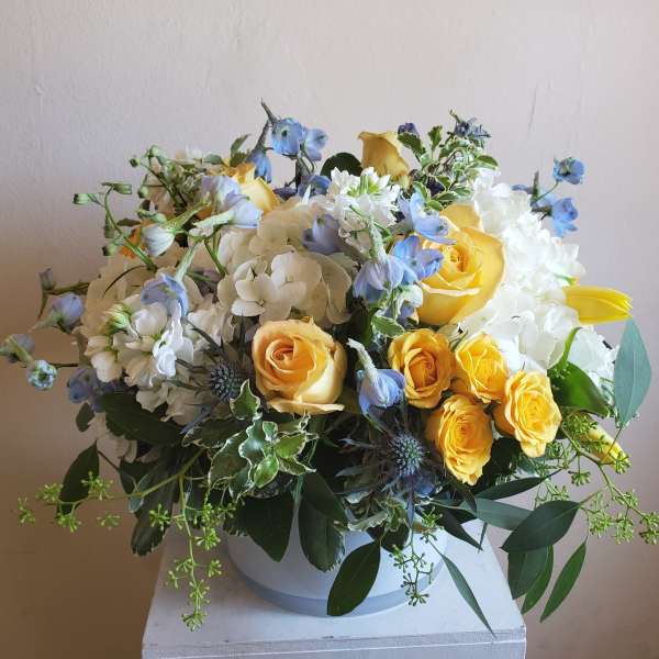 Bouquet of yellow roses, white hydrangeas, and blue flowers in a white vase