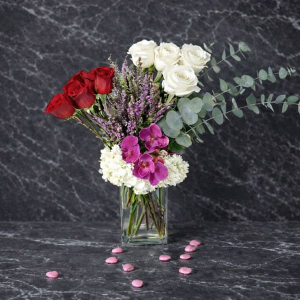 Bouquet of red and white roses with purple orchids in a glass vase