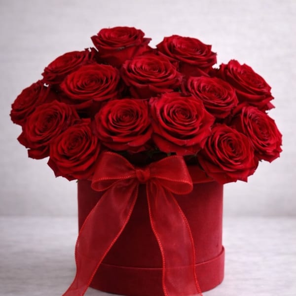 Red roses arranged in a round hatbox with a red ribbon bow