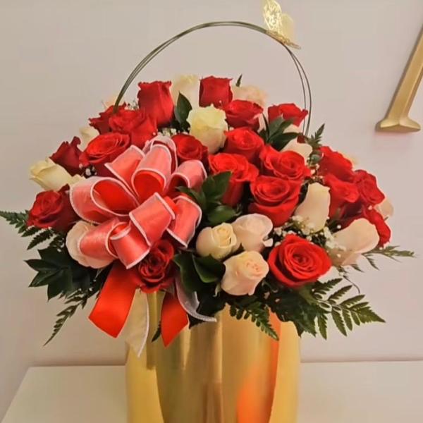 Arrangement of red and white roses in a tall gold vase with a ribbon bow and butterfly accent