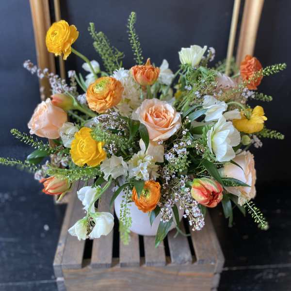 Mixed bouquet of peach, yellow, and white flowers in a white vase