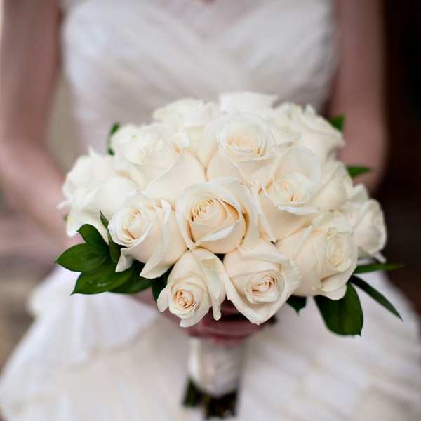 Hand-tied bouquet of ivory roses held by a person in a white strapless dress