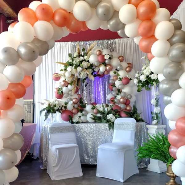 Balloon arch with white, peach, and silver balloons around floral displays