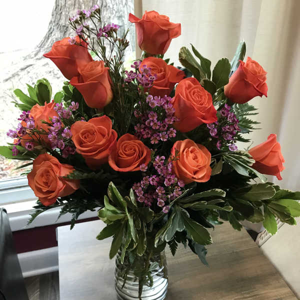 Orange roses and purple filler flowers in a clear glass vase