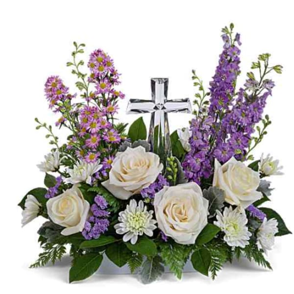 White roses and purple flowers arranged around a clear glass cross