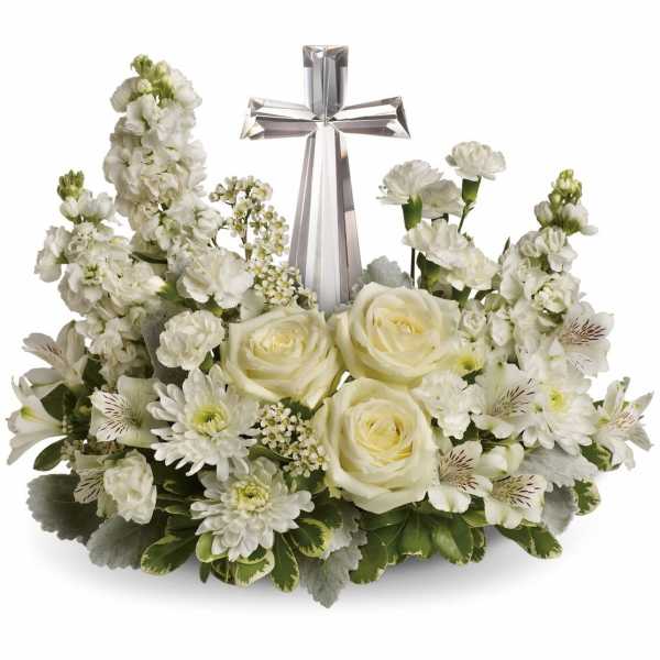 White floral arrangement with roses, carnations, and a crystal cross in a low container.