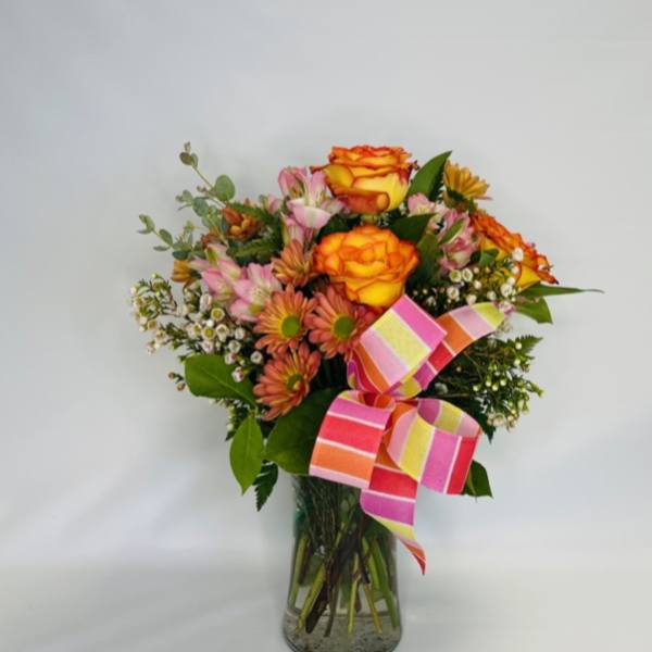 Bouquet of orange and pink flowers in a glass vase with a striped ribbon