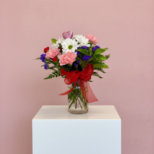 Bouquet of pink and white flowers in a glass vase with a red ribbon