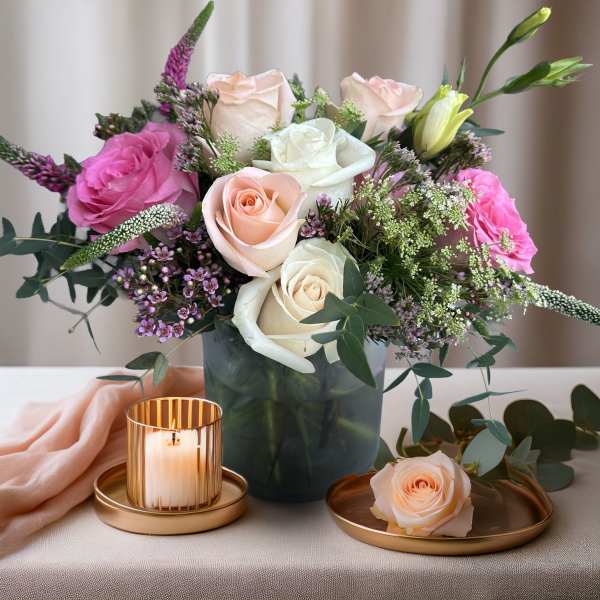 Bouquet of pink and white roses in a dark vase with a candle and single rose