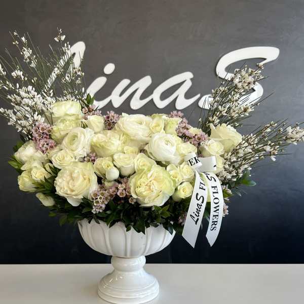 White rose arrangement in a white pedestal vase with a ribbon