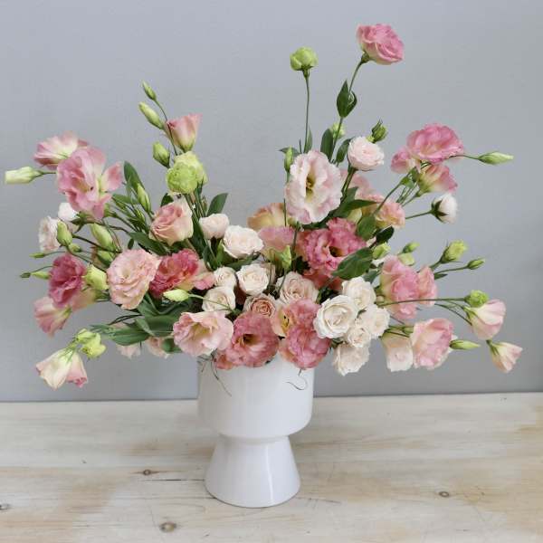 Low wide arrangement of pink lisianthus and blush spray roses in a modern white ceramic vase