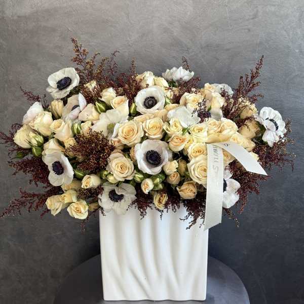 Cream roses and white anemones arranged in a white vase