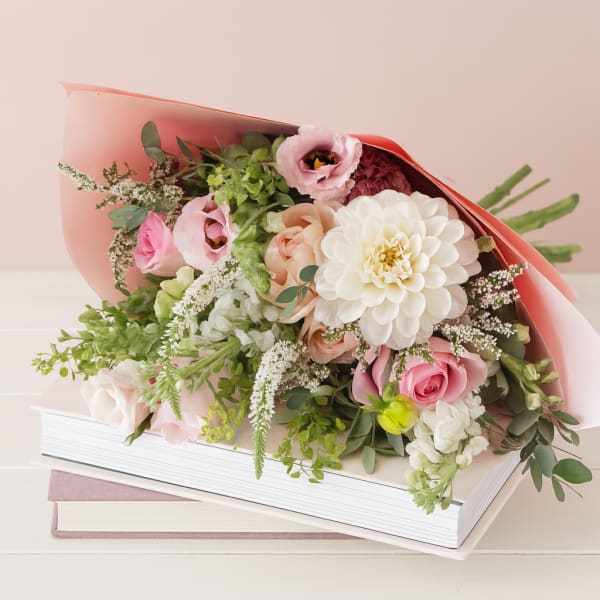 Pink and white bouquet wrapped in coral paper, resting on books