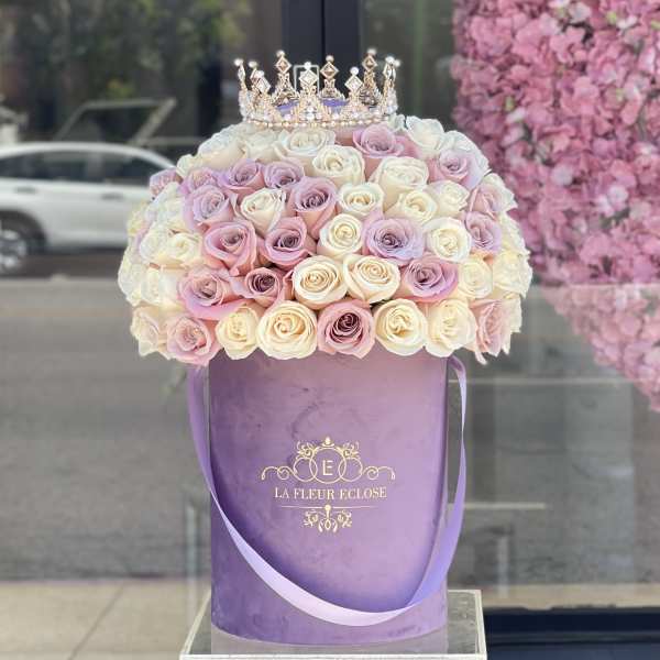 Pastel roses arranged in a purple hatbox with a jeweled crown on top