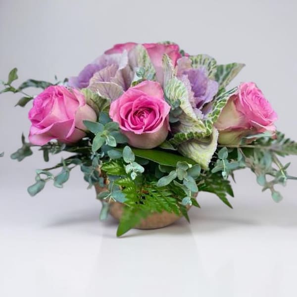 Pink roses arranged with variegated foliage in a low vase