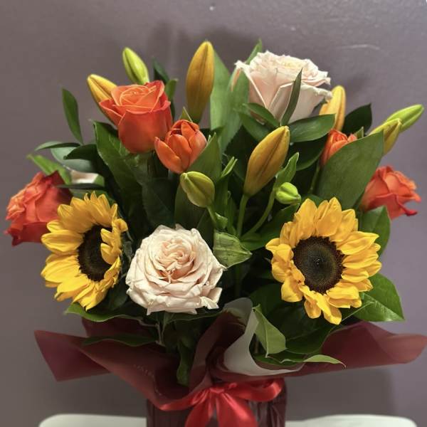 Bouquet of roses, sunflowers, and lilies in a wrapped container