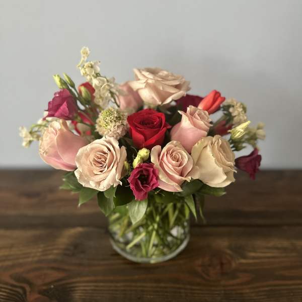 Low bouquet of blush pink and red roses with accent blooms in a clear glass vase