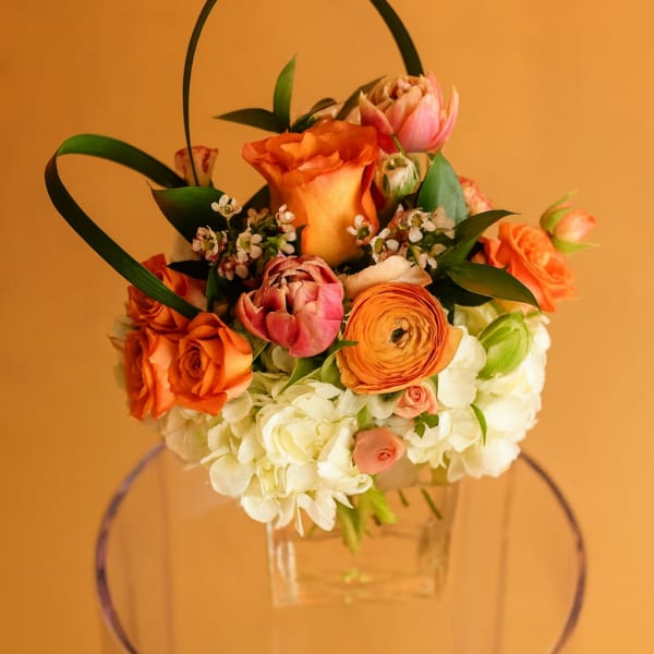 Orange and pink floral basket arrangement in a clear container