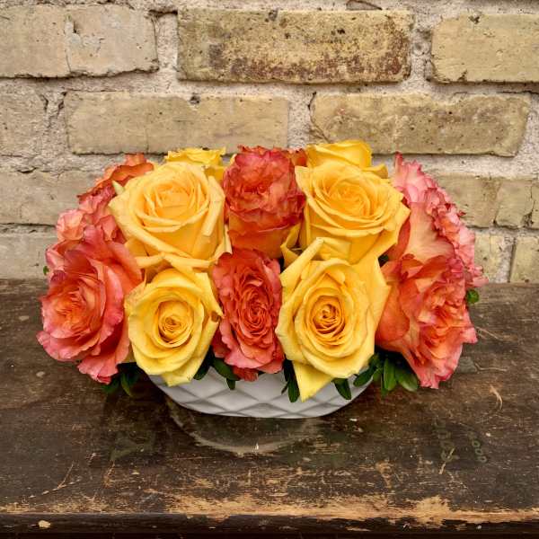 Yellow and coral roses arranged in a white bowl vase