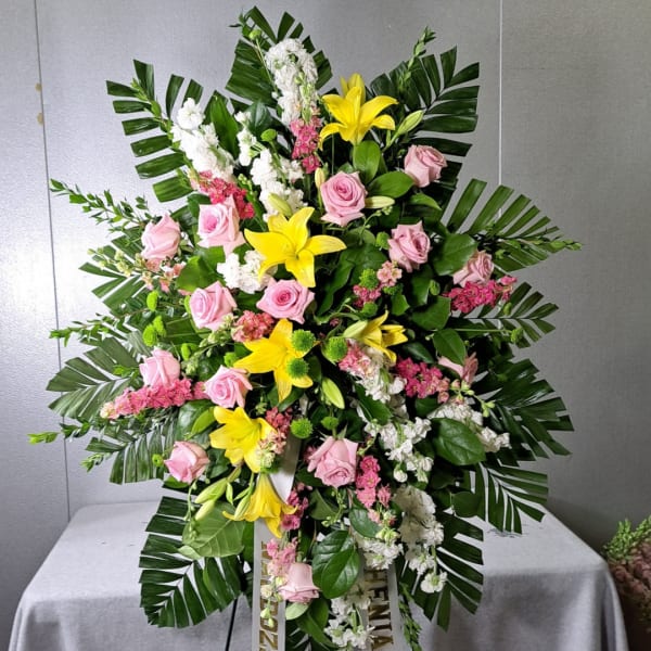 Standing floral spray with pink roses, yellow lilies, and white blooms