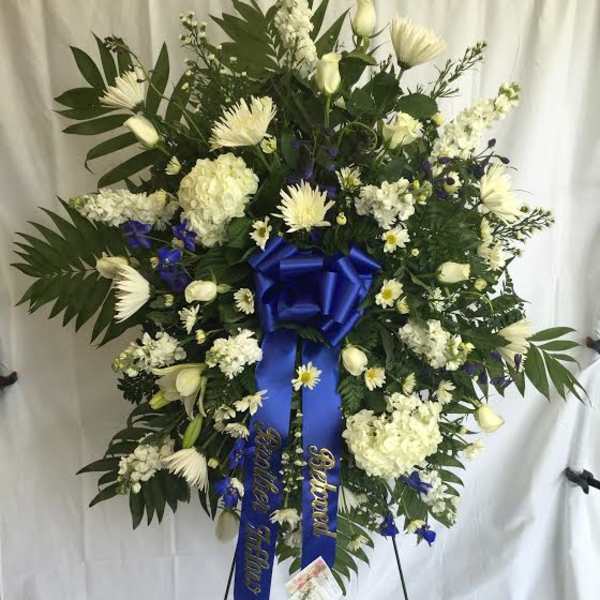 Large white floral standing wreath with blue ribbon on an easel