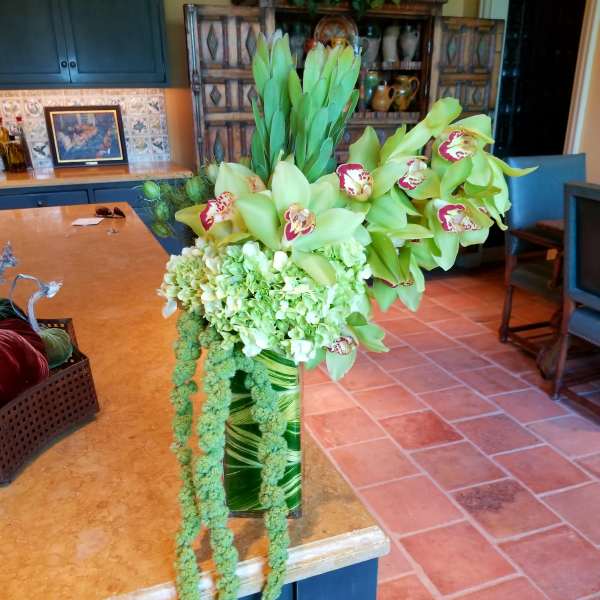 Tall green floral arrangement with orchids and hanging amaranthus in a glass vase