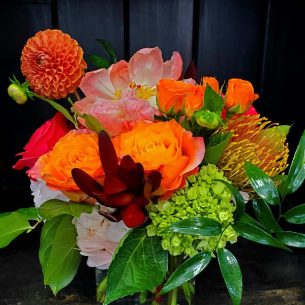 Bright mixed bouquet of orange, pink, and green flowers in a glass vase