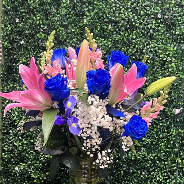 Bouquet of pink lilies, blue roses, and white baby's breath in a glass vase