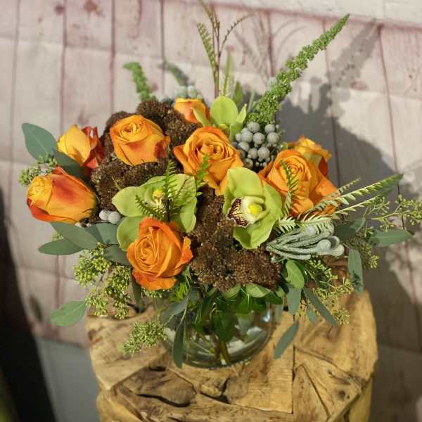 Orange roses and green orchids arranged in a glass vase