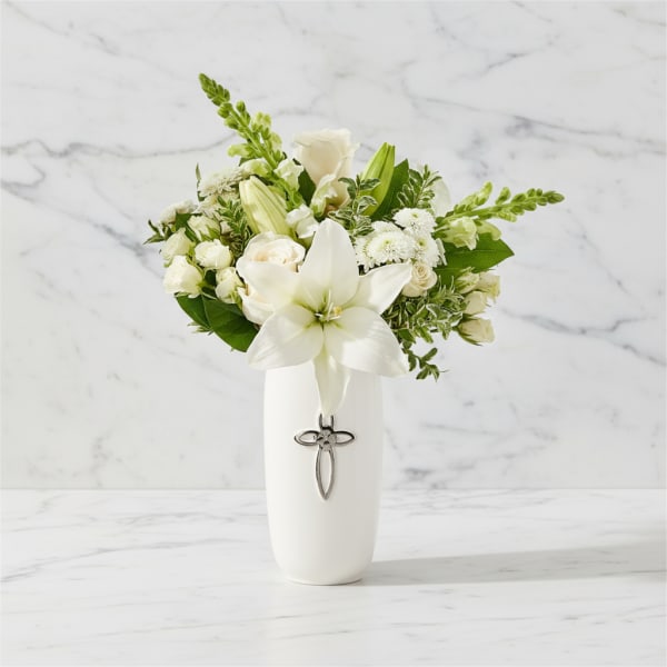 White lily and rose arrangement in a white vase with a cross charm