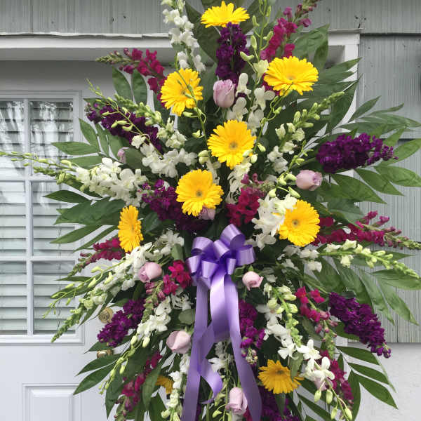 Standing floral spray with yellow daisies, purple and white blooms, and a lavender ribbon