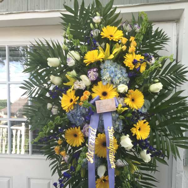 Large standing floral wreath with yellow daisies and blue flowers