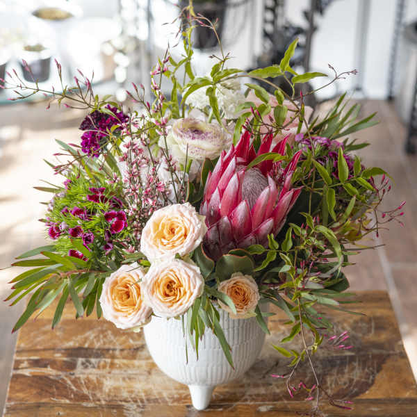 Mixed bouquet with peach roses, pink protea, and white blooms in a white vase