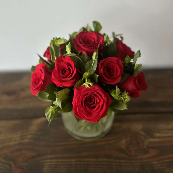 Compact arrangement of red roses in a clear glass vase on a wooden surface