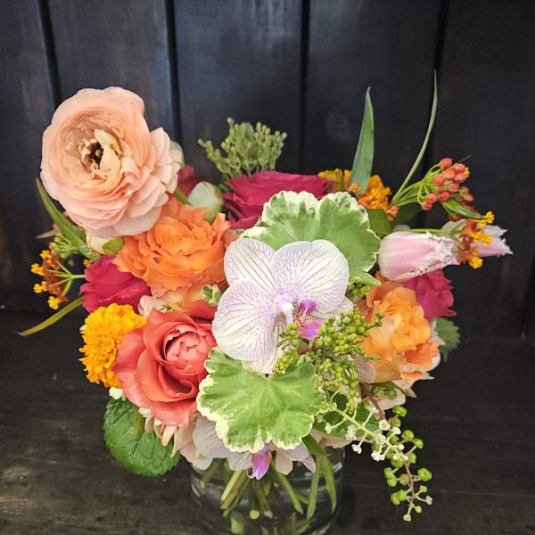 Mixed bouquet of roses, orchids, and ranunculus in a glass vase
